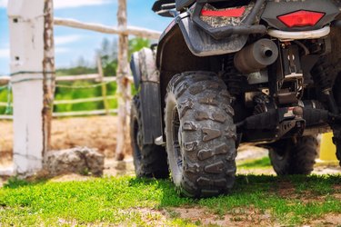 ATV quad bike vehicle standing near wooden fence at farm or horse stable. Back view of all wheel drive motorcycle at farm. Rural countryside machine